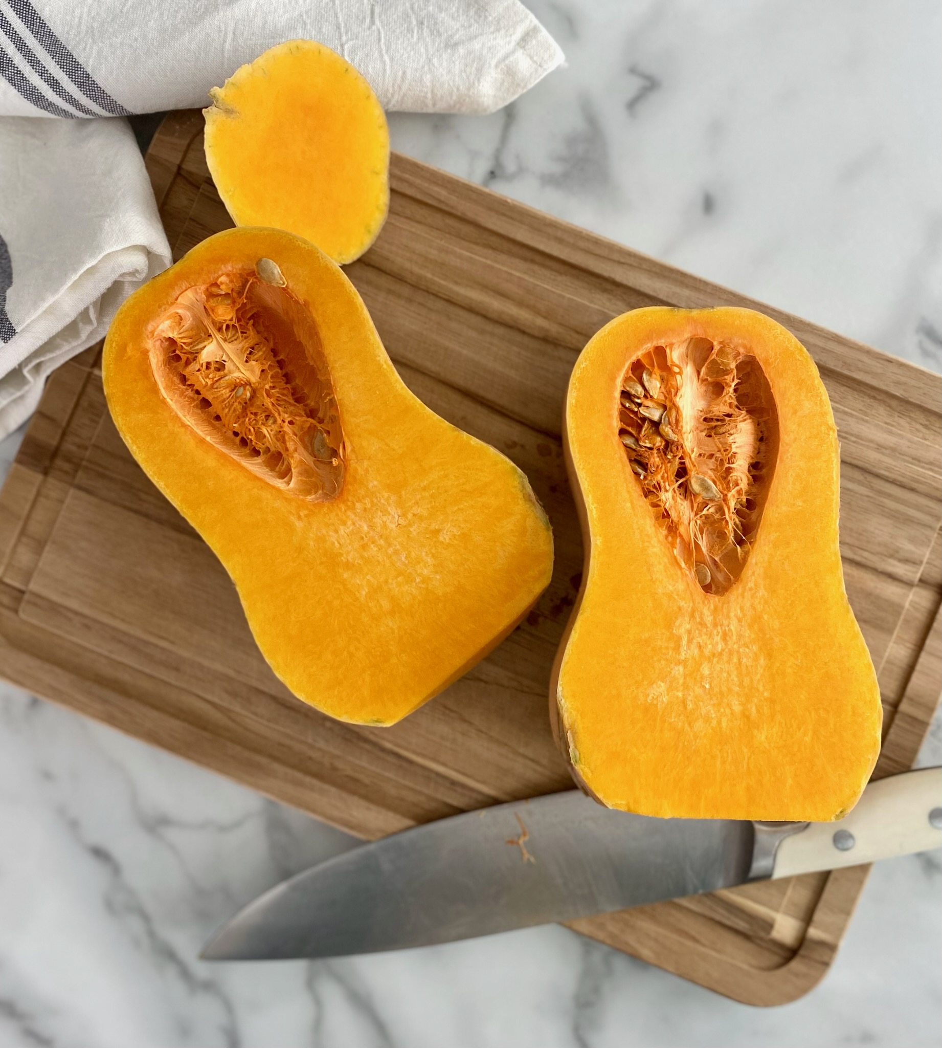two halves of butternut squash and a knife on a cutting board