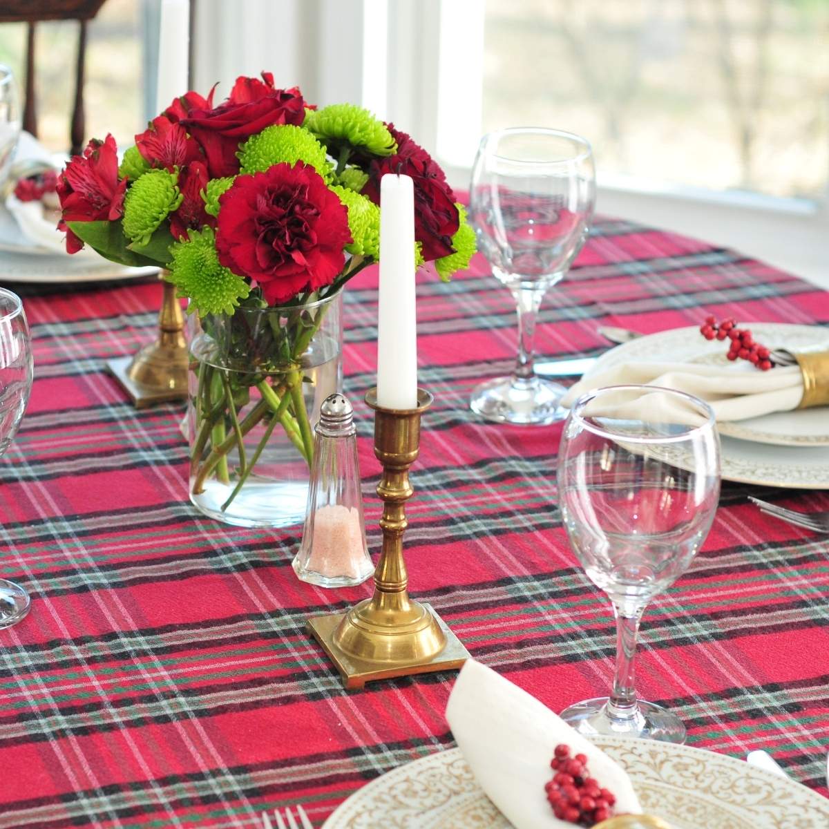 red and green bouquet with taper candles on a plaid tablecloth