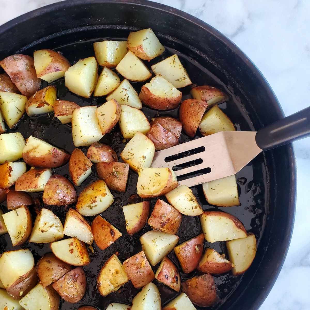 garlic and herb roasted potatoes in a pan with a serving utensil