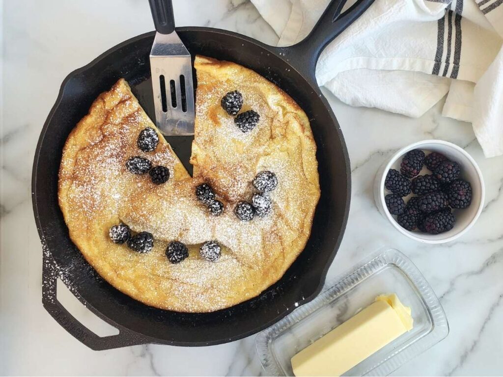 sourdough german pancake with blackberries and powdered sugar in a cast iron skillet